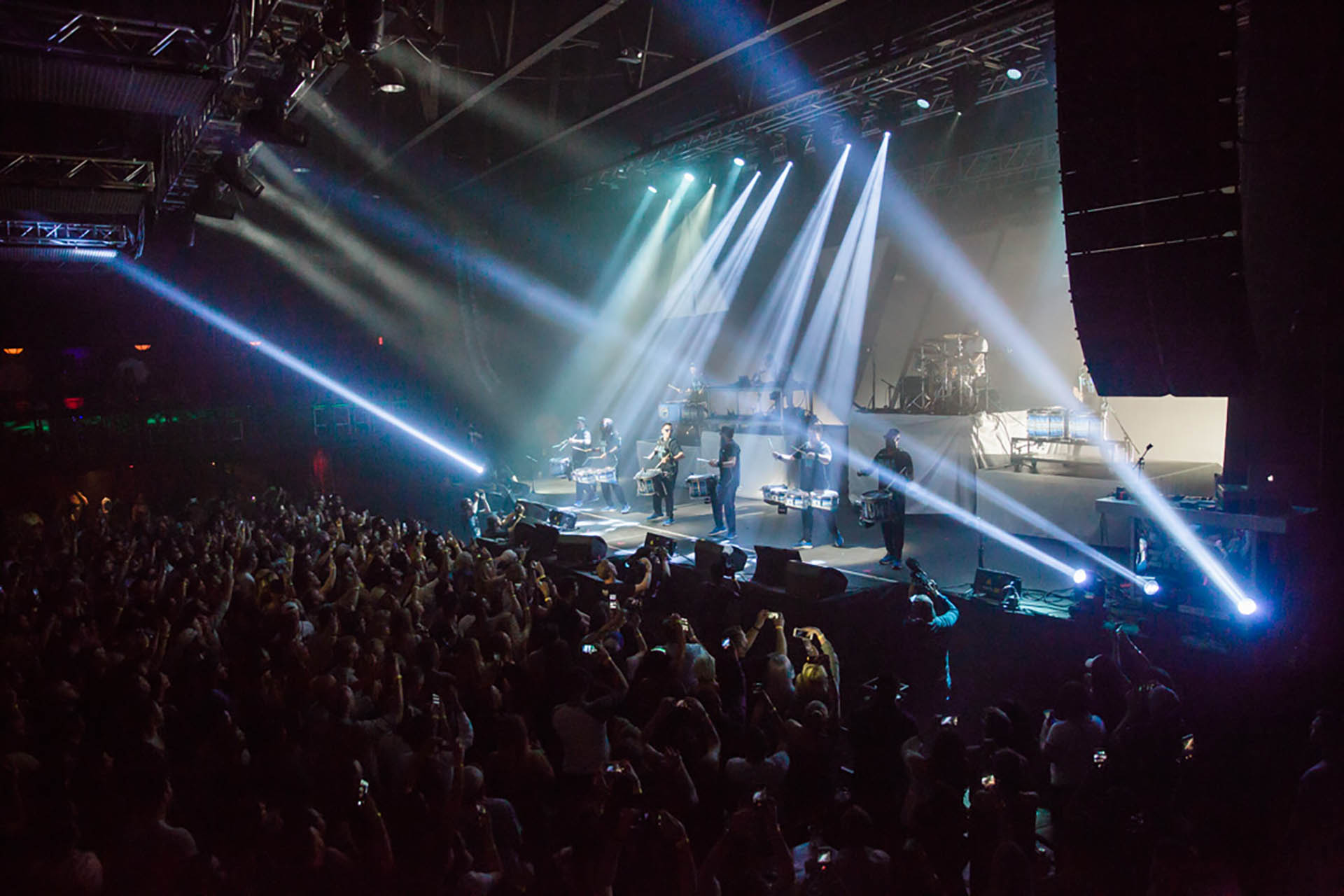 DFW live event photography; wide photo of a musical group performing on stage surrounded by many spotlights pointing in many directions. A large crowd is seen enjoying the performance in the foreground.