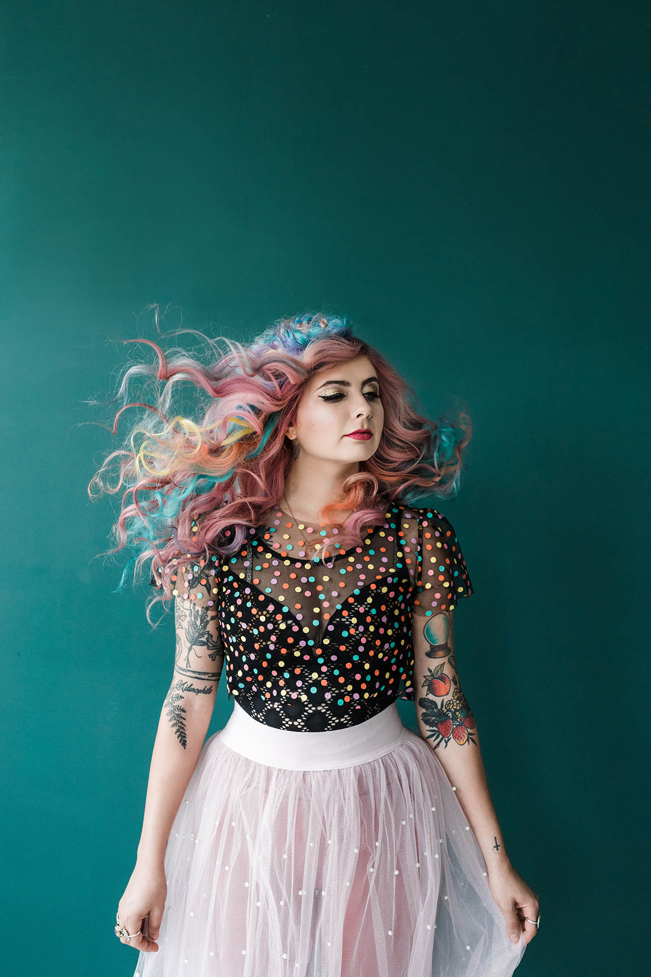 Dallas Commercial Photography; a woman with flowing multi-colored hair wearing elaborate makeup and a colorful, polka dotted top looking off into the distnace in front of a blue background