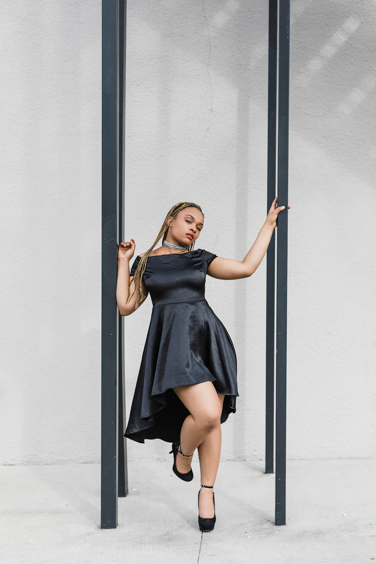 Inclusive fashion photos; photo of an African American woman in a black dress posing alluringly between a black metal frame in front of a white background