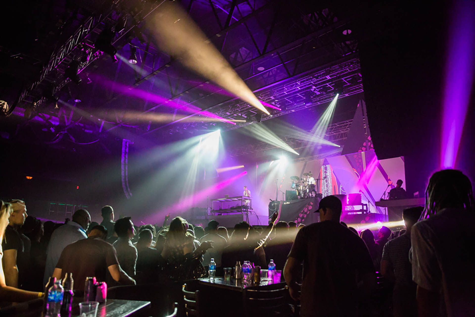 Live music photos of a concert in DFW. The stage is covered in purple light while colorful spotlights point in multiple directions including hightling the audience.