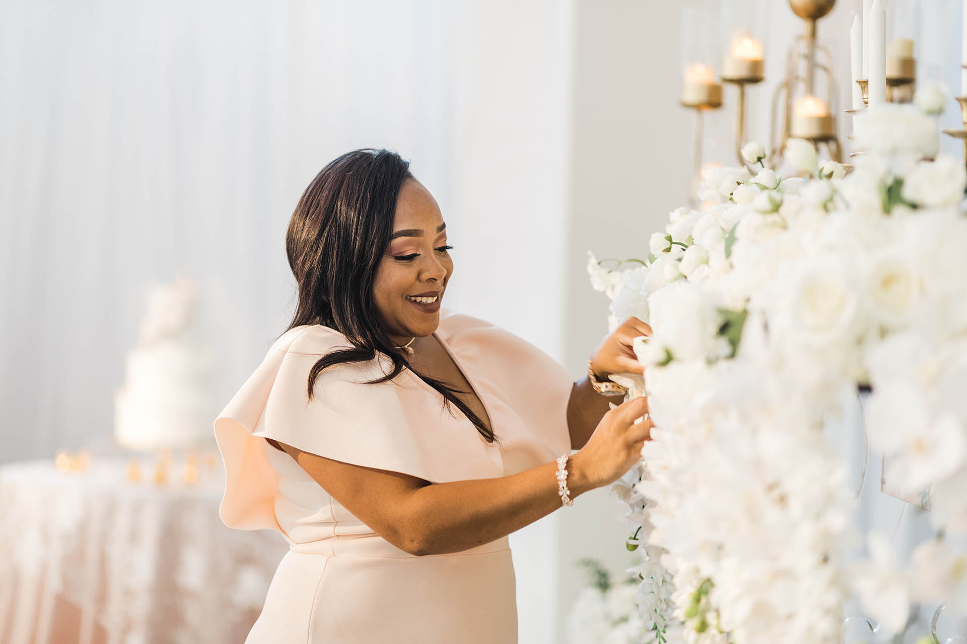Brand photography; African American woman in a fashionable dress working on a white floral arrangement with a wedding cake in the background