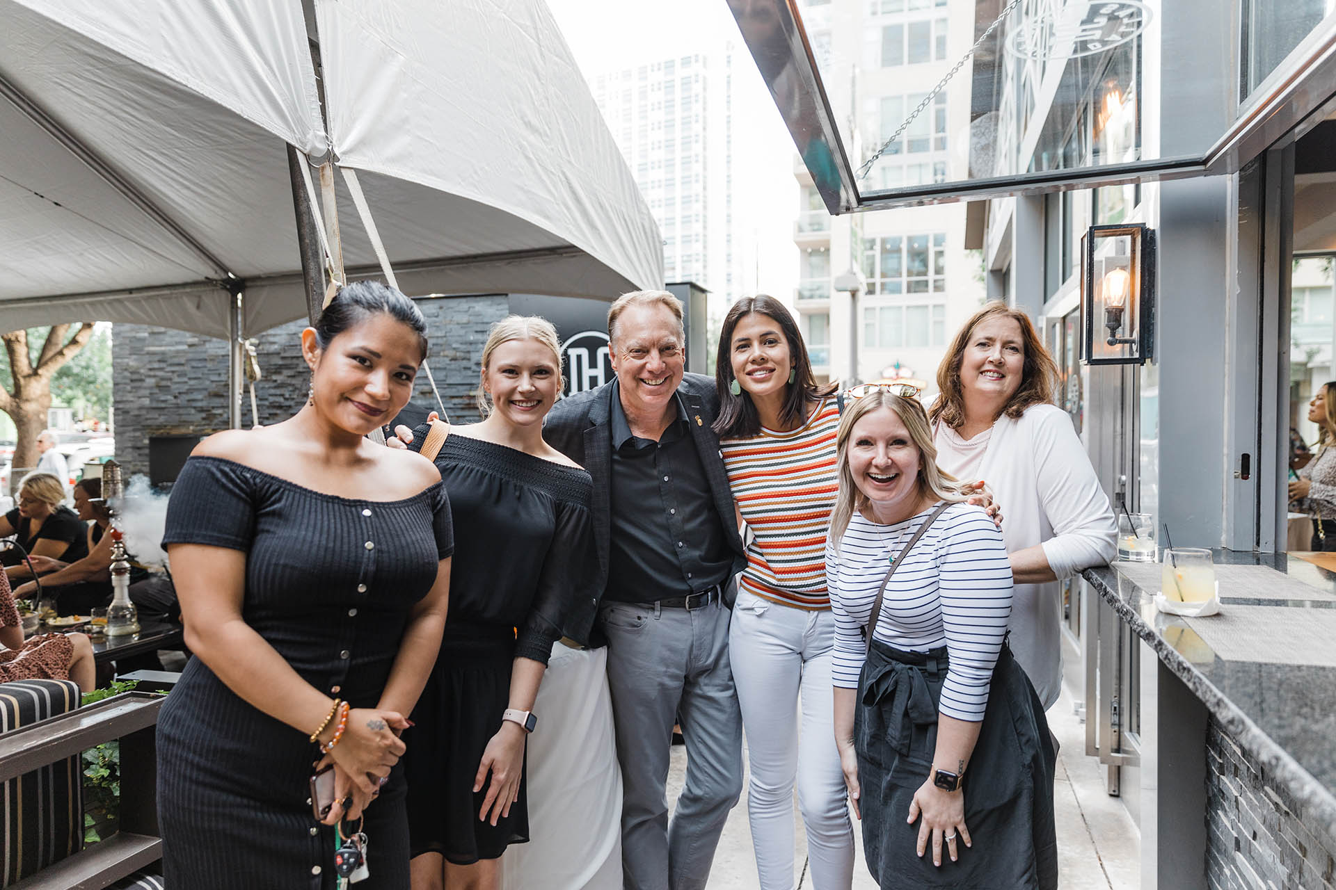 Corporate group photography of five women and one man casually smiling and posing together at an outdoor event in Fort Worth.