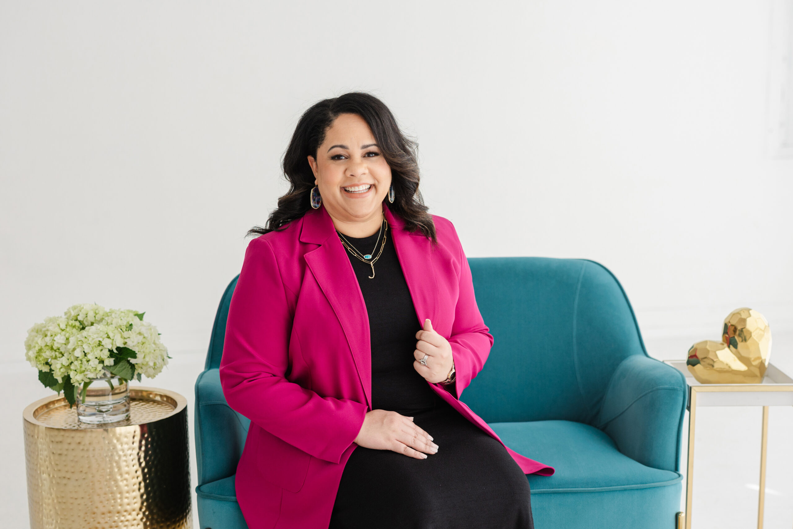 a woman in a pink blazer sitting on a blue sofa for her professional business branding photography session