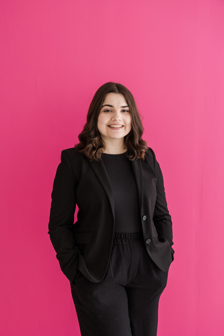 Colorful Dallas Headshots; photo of woman in all black smiling in front of a colorful pink background