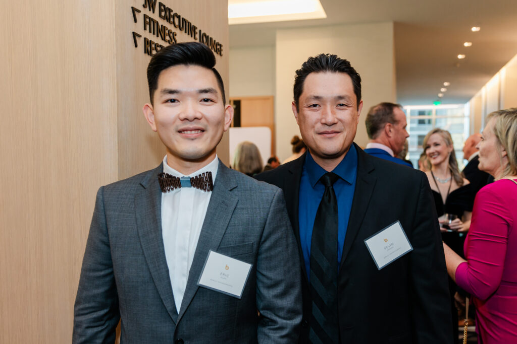 two men standing next to each other and smiling at a corporate event in dallas
