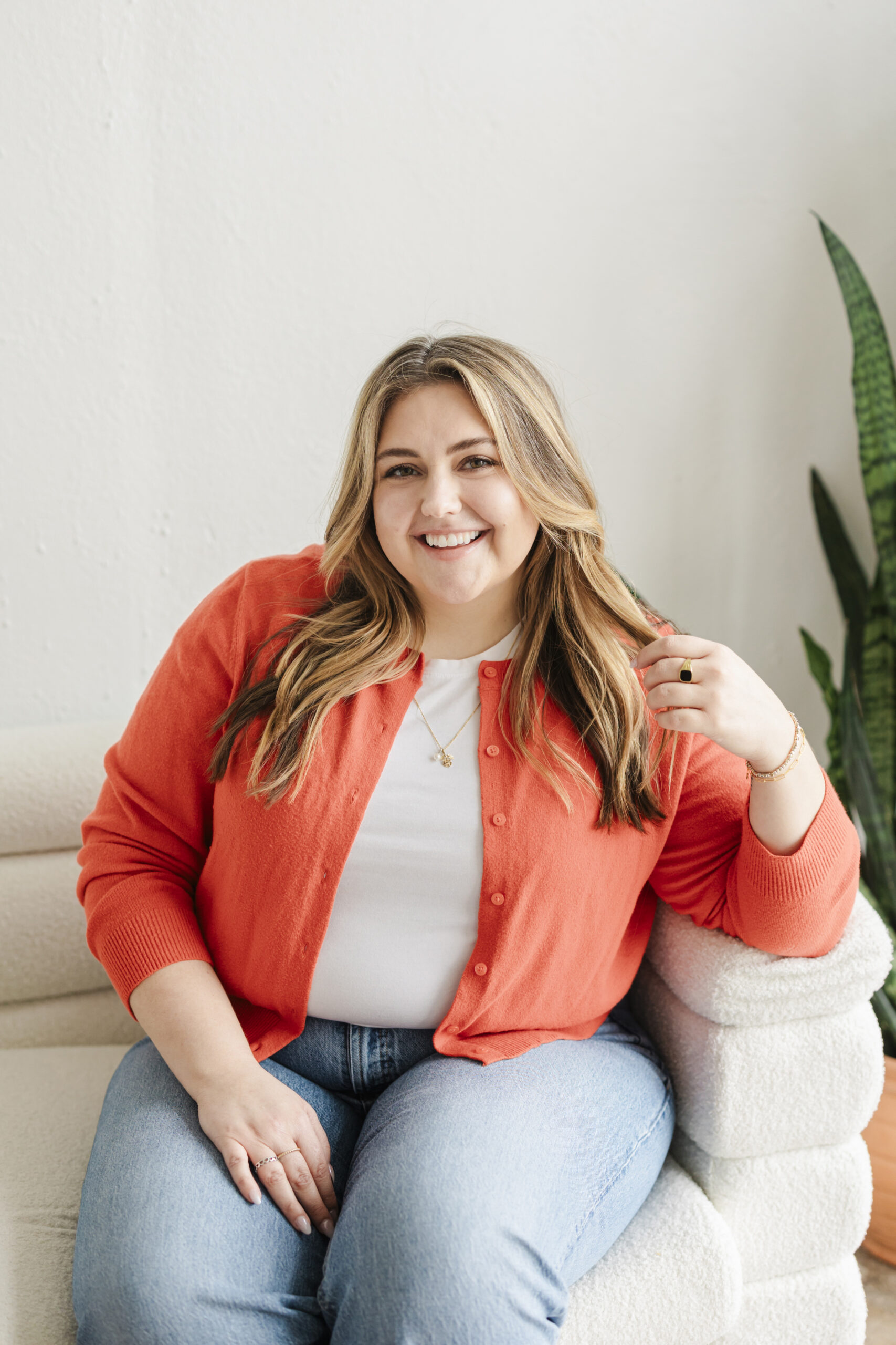 a woman wearing an orange cardigan sitting on a white couch taking lifestyle headshots 