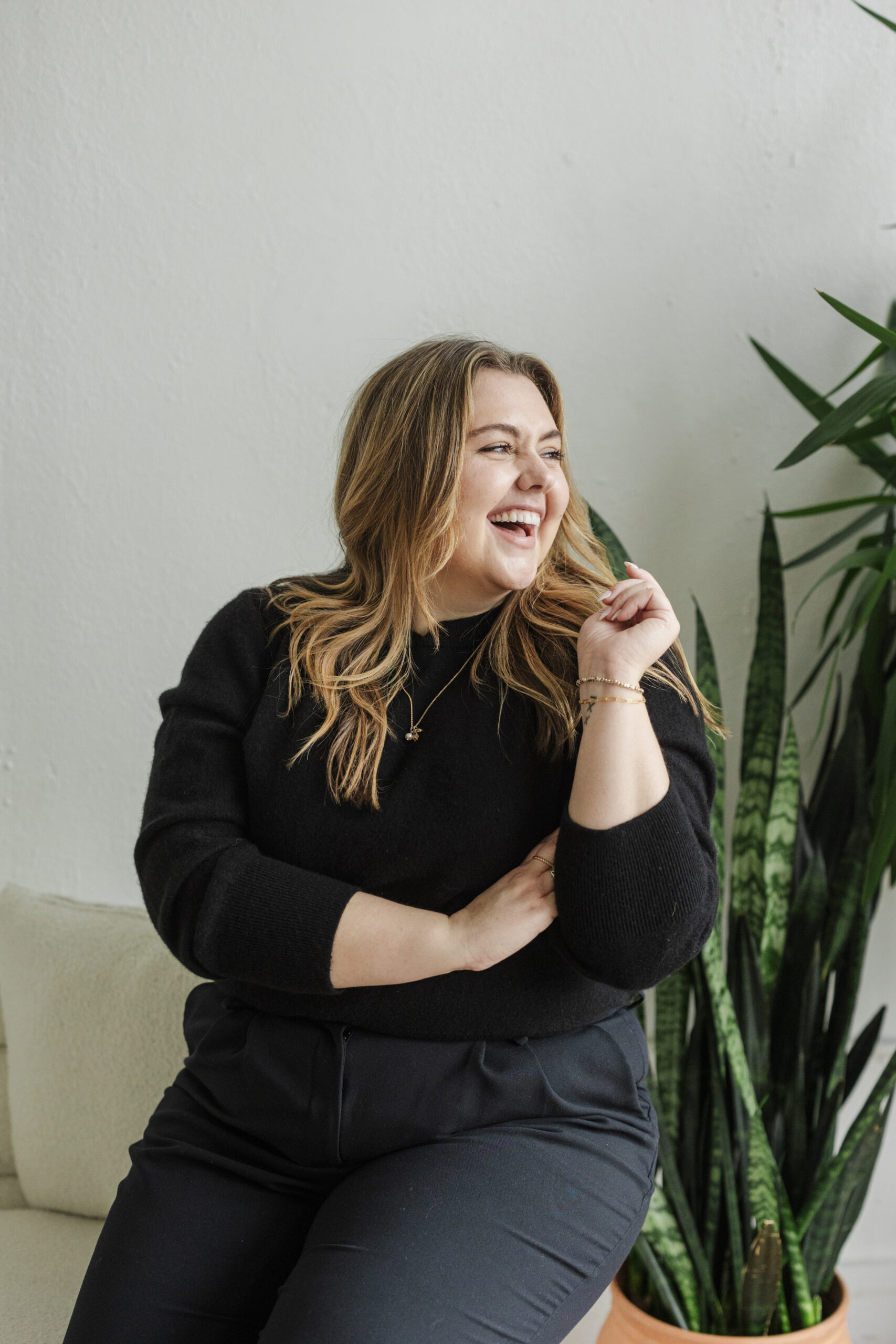 a woman wearing a black sweater sitting on a couch in a studio taking lifestyle headshots 