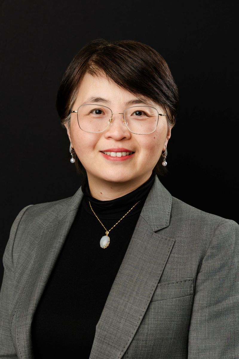 a woman wearing a blazer taking corporate headshots in dallas against a black backdop 