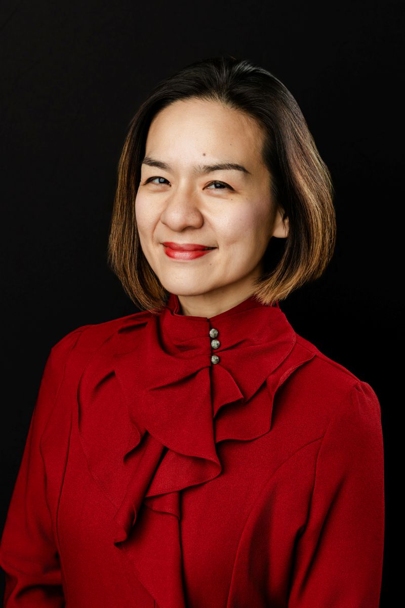 a woman wearing a red blouse taking corporate headshots in dallas against a black backdop 