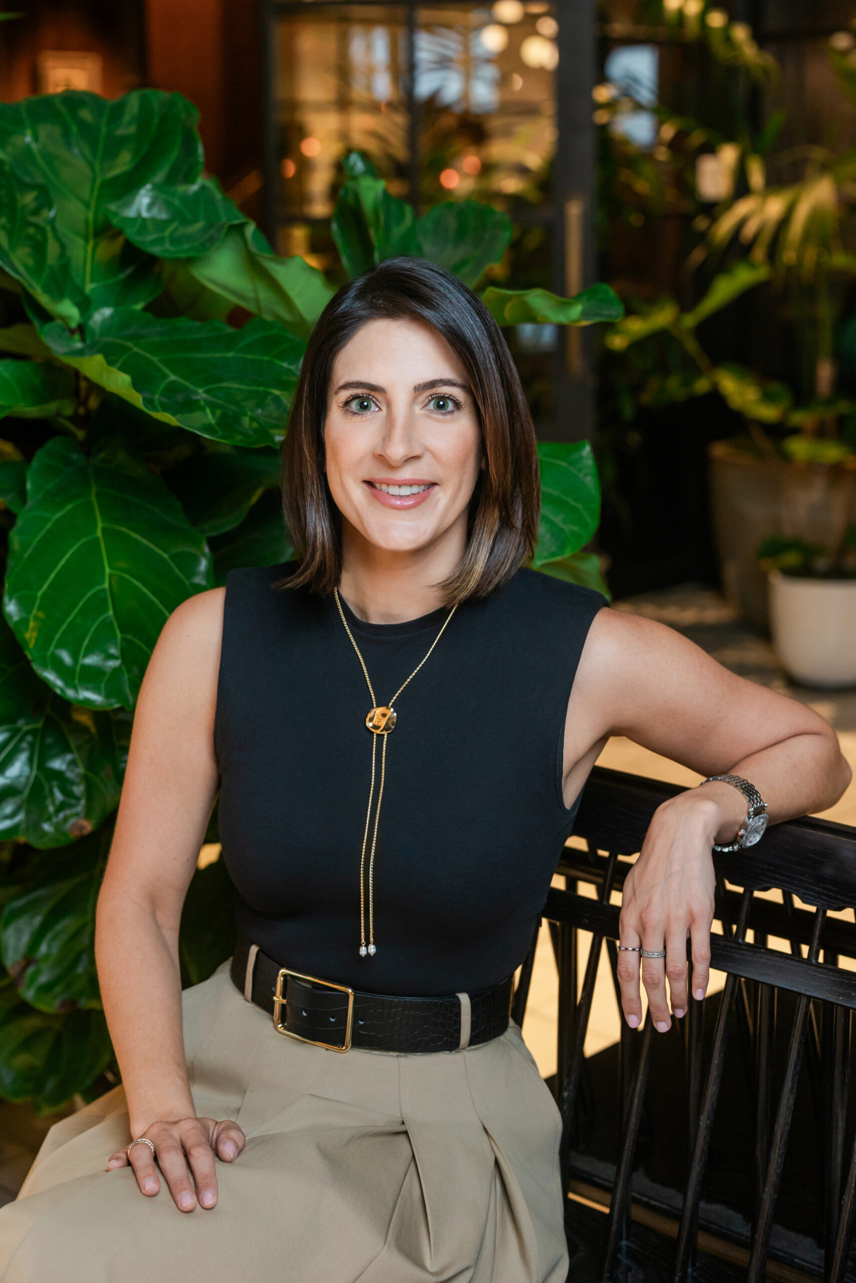 a woman sitting on a bench in front of plant taking a formal, corporate headshot  