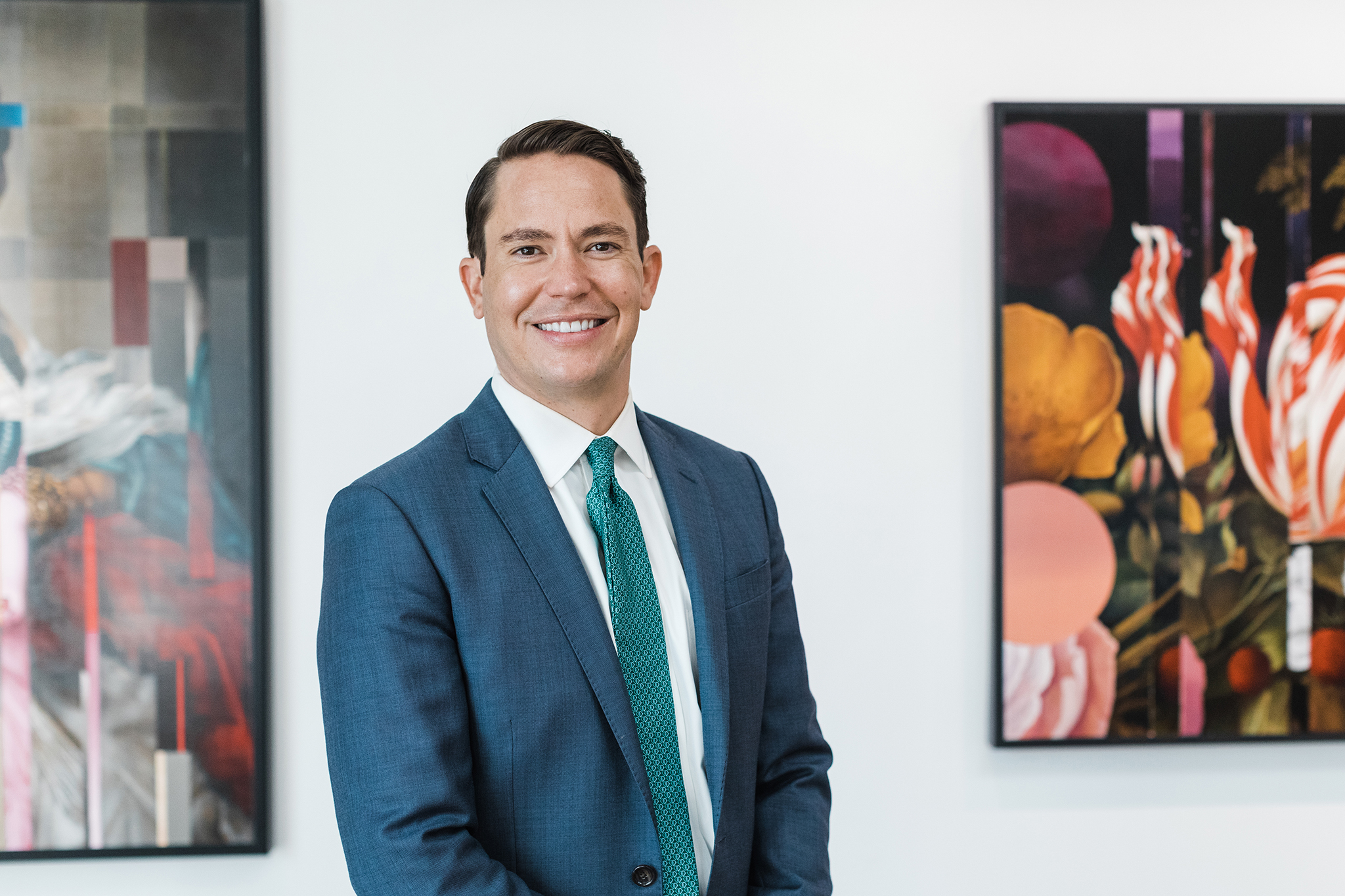 Dallas Headshots photo of a man in a blue suit in front of a white background surrounded by two paintings
