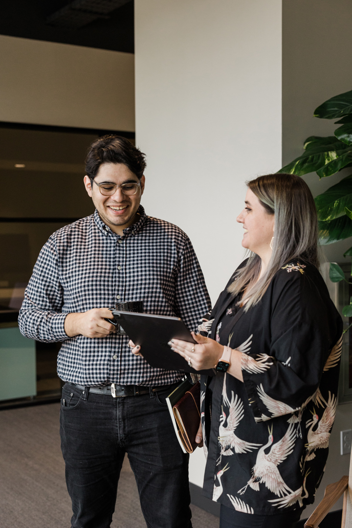 Dallas Corporate Lifestyle Photographer; candid shot of a man and woman in business casual attire smiling and looking at a tablet in an office setting