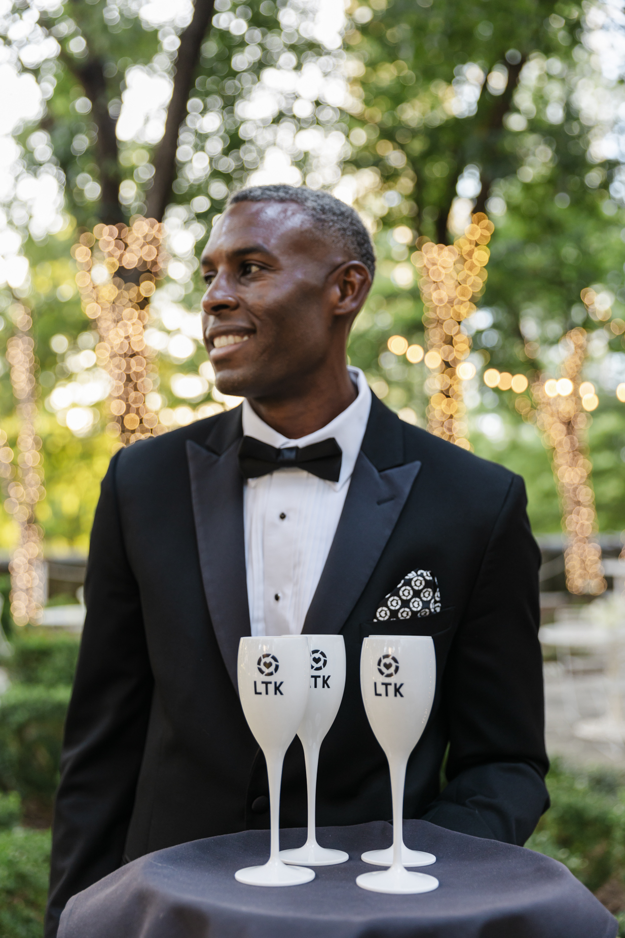 Dallas event photographer: photo of a worker in a tuxedo carrying a tray of drinks with the company's logo on the glasses.