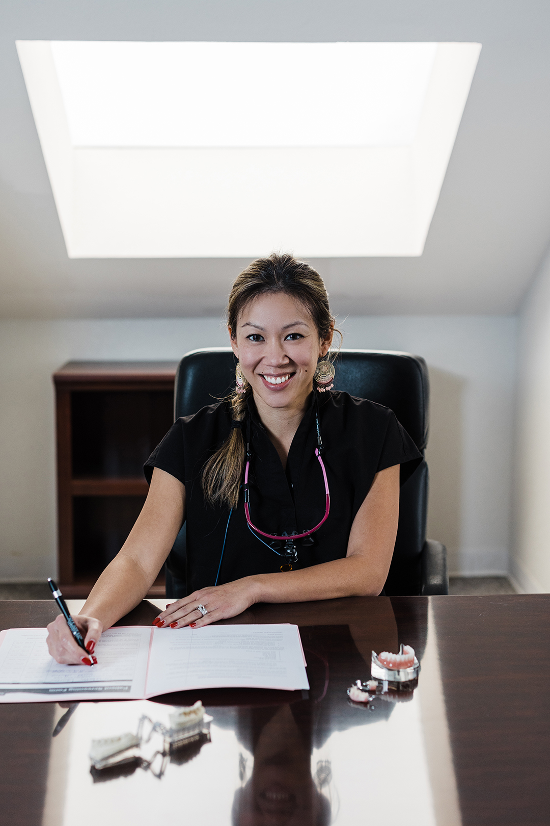 Dallas Fort Worth Brand Photographer; dentist in all black smiling while filling out paperwork at her desk