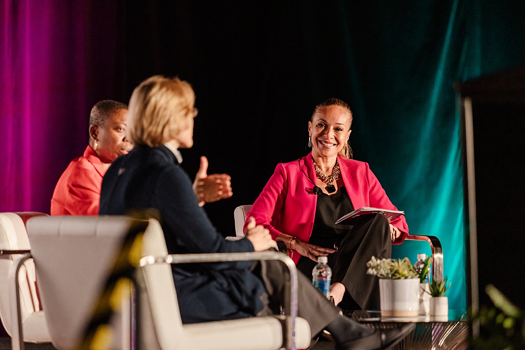 Dallas Fort Worth Event Photographer: three women sitting on chairs around a table on stage during the Forte Foundation's MBA Women's Leadership Conference in Dallas, Texas. All three women are wearing a professional business attire and are having a discussion.