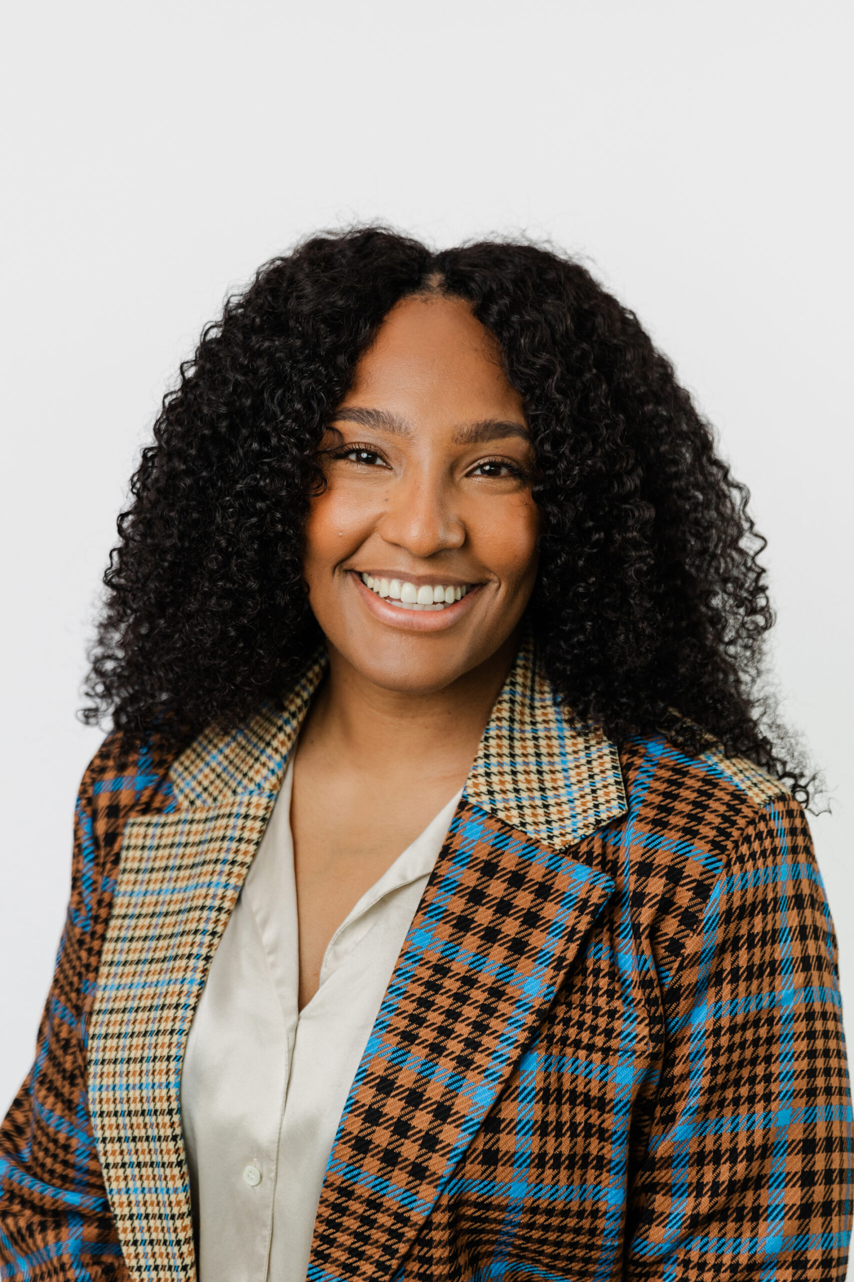 Dallas Fort Worth Headshot Photographer: a headshot of a corporate female employee in front of a white background. She's wearing a light colored top and a colorful, plaid jacket.