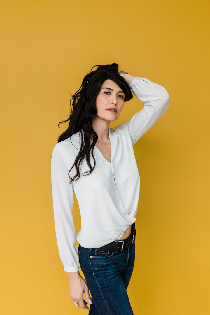 Dallas Fort Worth Model Headshot Photographer; woman in a white shirt and jeans posing alluringly in front of a yellow background