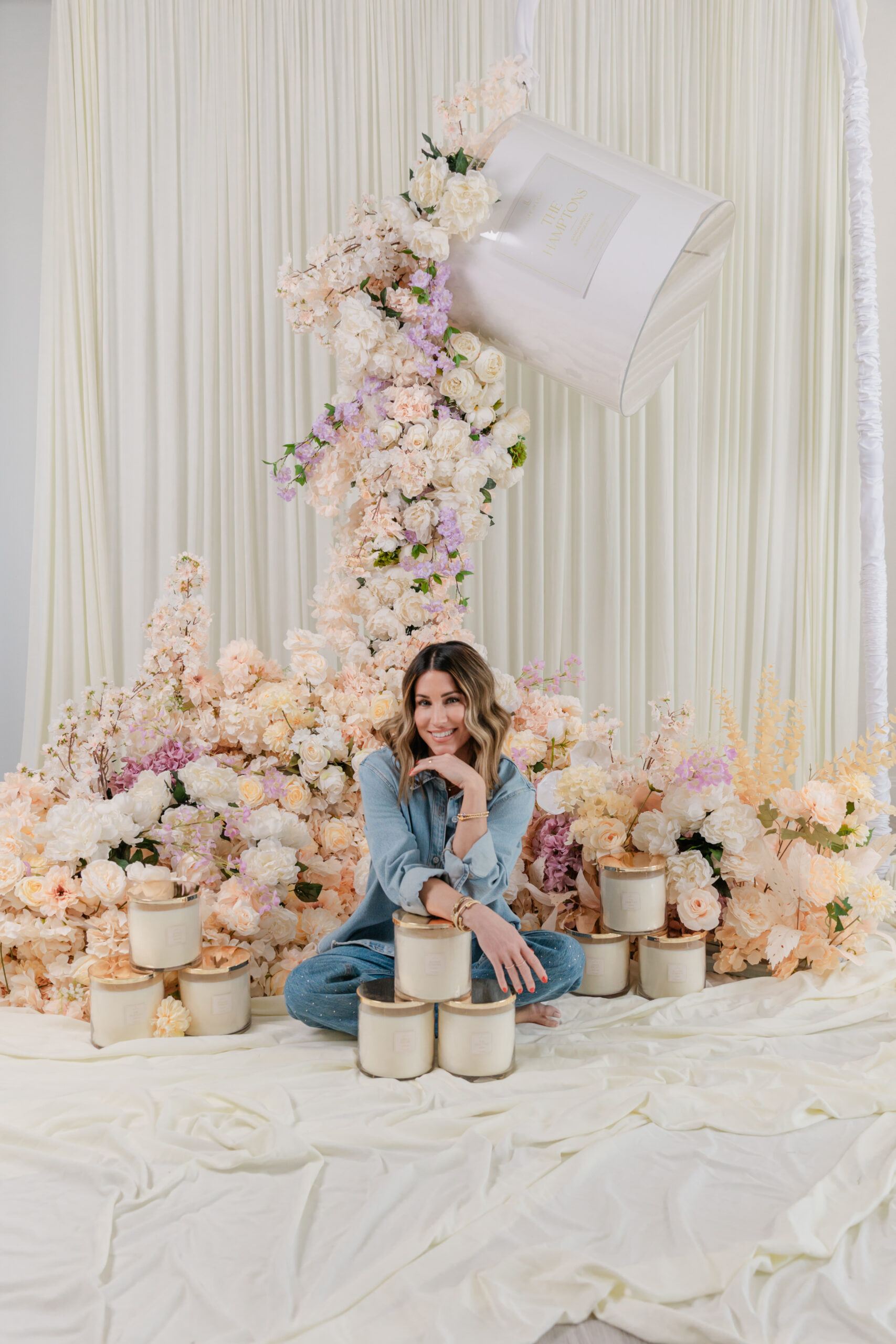the founder of Life In Lilac sitting on the ground next to their candles behind her is a large floral display 