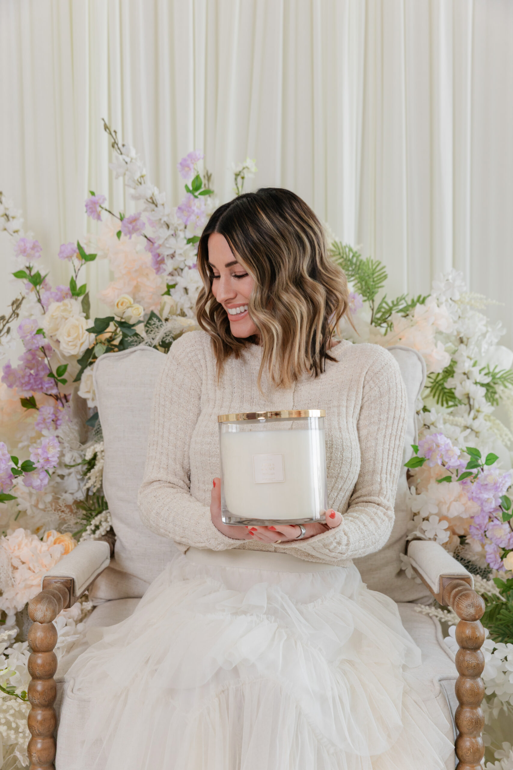 the founder of Life In Lilac is sitting on a white chair and holding one of her candles 