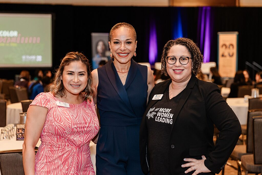 Three women smiling and posing together during the Forte Foundation's MBA Women's Leadership Conference in Dallas, Texas. All three women are dressed in varying types of professional business attire and have on Forte branded name tags.