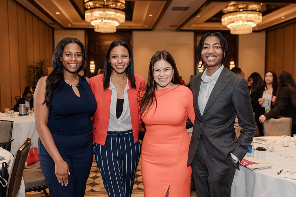 Four women smiling and posing together during the Forte Foundation's MBA Women's Leadership Conference in Dallas, Texas. All four women are dressed in varying types of professional business attire.