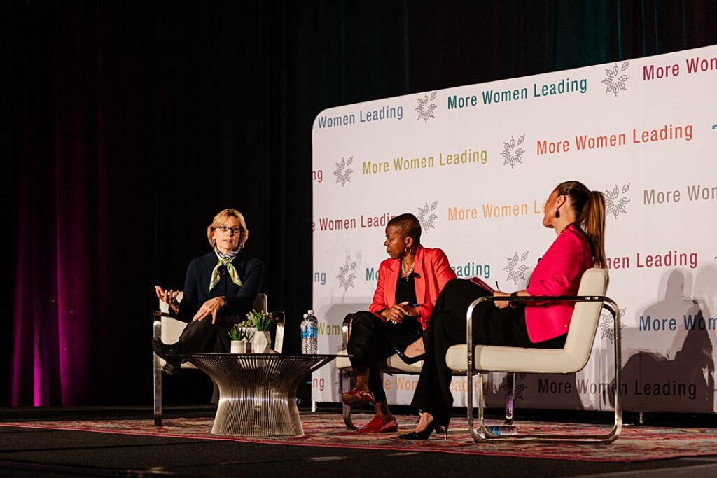 Three women sitting on chairs around a table on stage during the Forte Foundation's MBA Women's Leadership Conference in Dallas, Texas. All three women are wearing a professional business attire and are having a discussion.