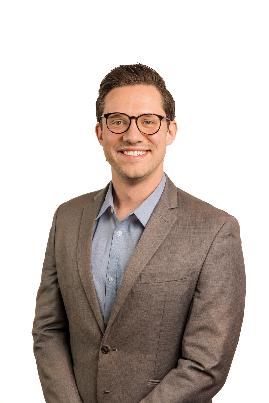 a man with glasses and a tan blazer takes a corporate headshot against a white backdrop