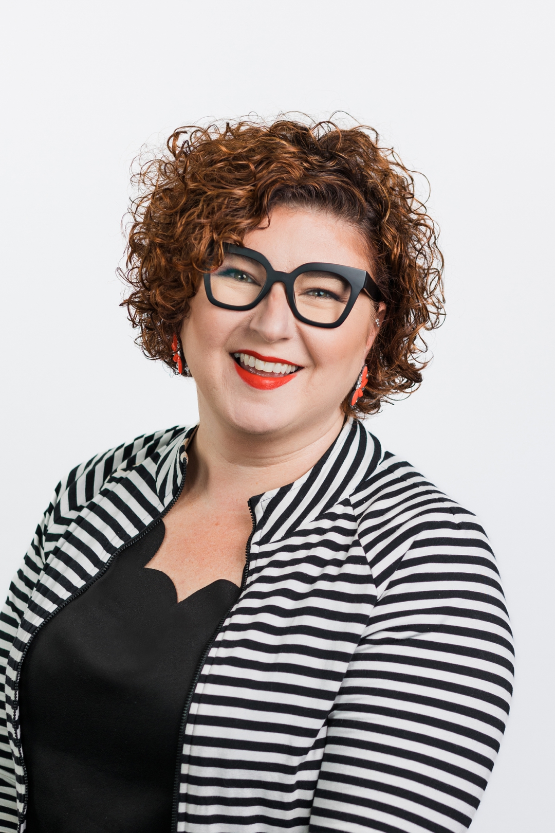 a woman with short curly hair and glasses takes a corporate headshot wearing a striped blazer