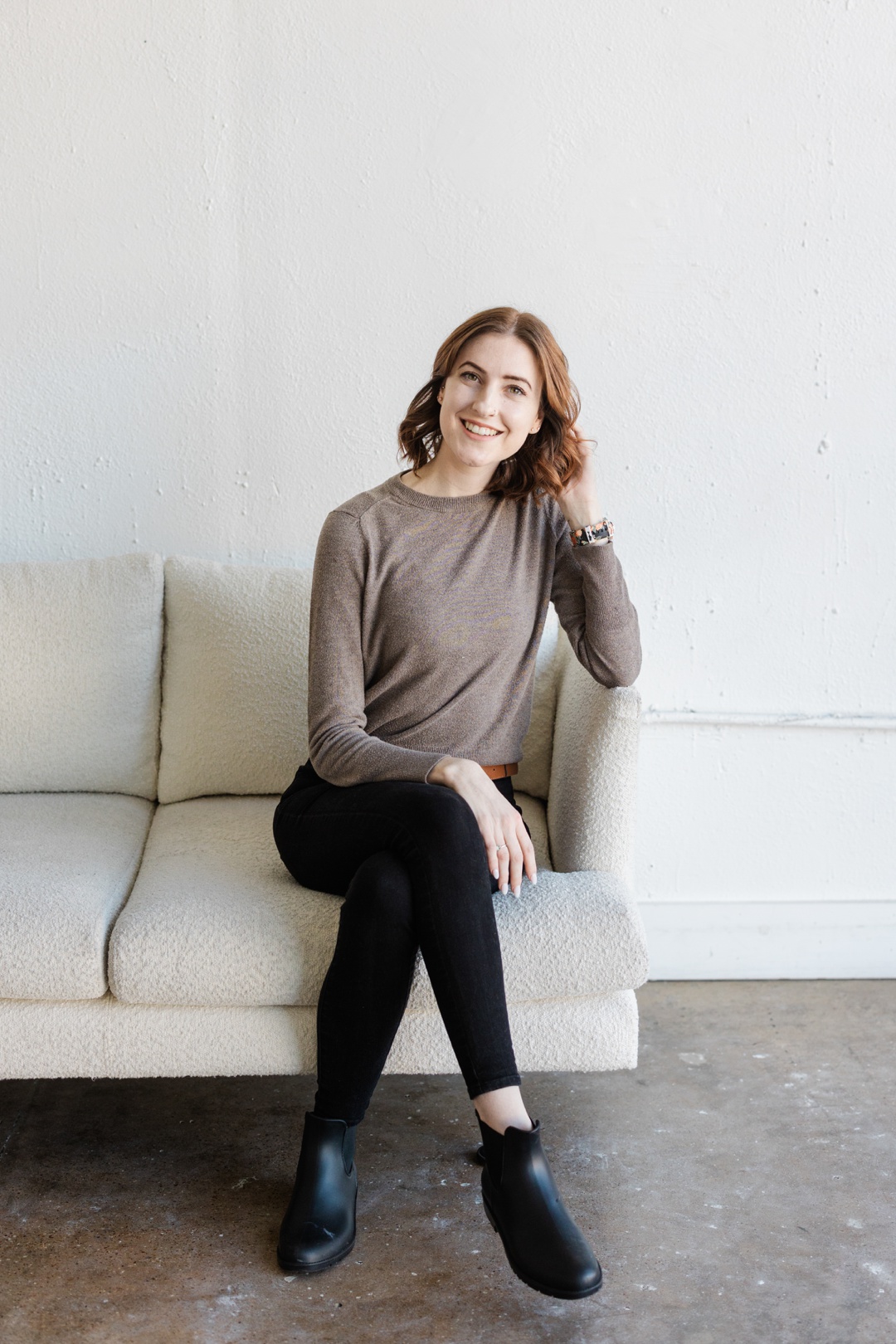 A smiling woman sitting on a white couch in front of a white wall