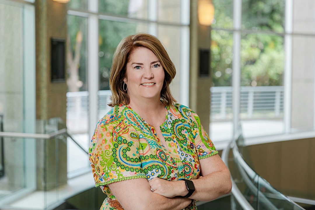 DFW Event Photographer: a portrait of the CEO during the Forte Foundation's MBA Women's Leadership Conference in Dallas, Texas. She's wearing a colorful, paisley dress and is smiling with crossed arms.