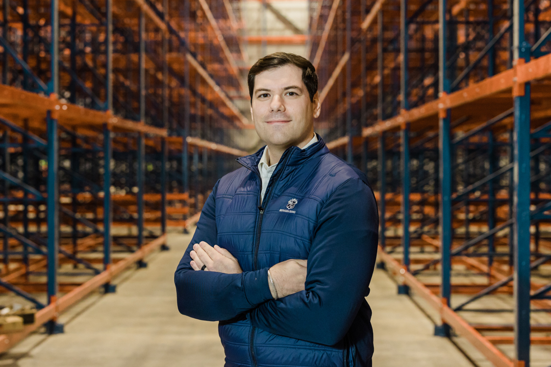 DFW Headshot Photographer; man in a blue jacket smiling subtly with crossed arms in a large, cold storage facility