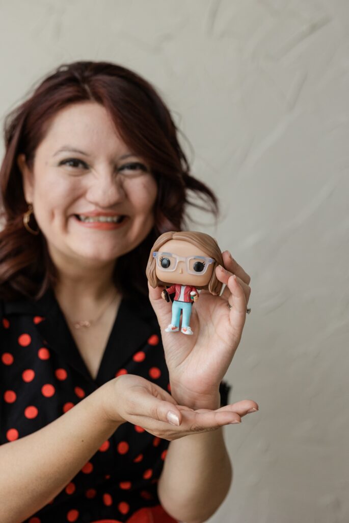 Latina woman wearing a black and red polka dotted dress while holding a FUNKO Pop figurine