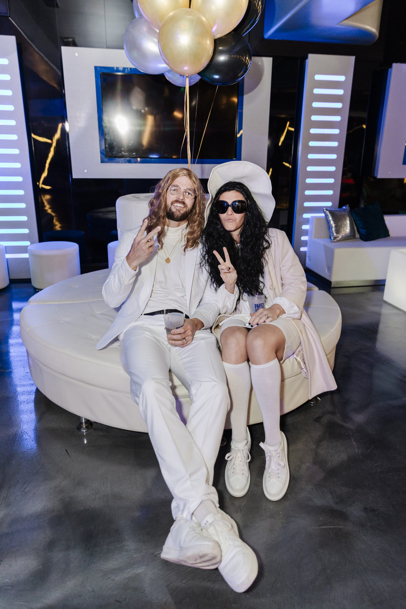 a man and woman sitting on a sofa and holding up peace signs