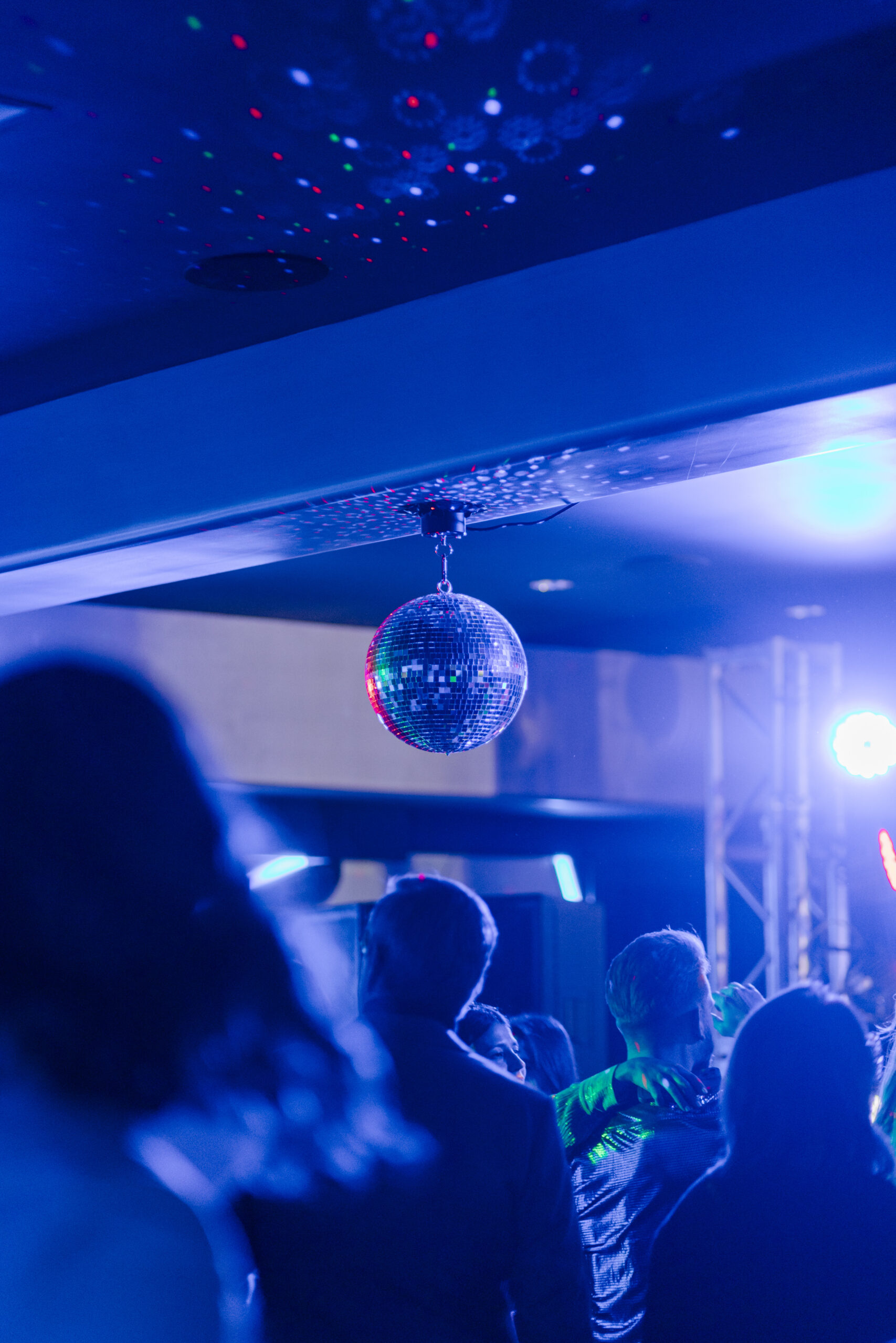 a disco ball hanging from a ceiling as a group of people dances together on a dance floor