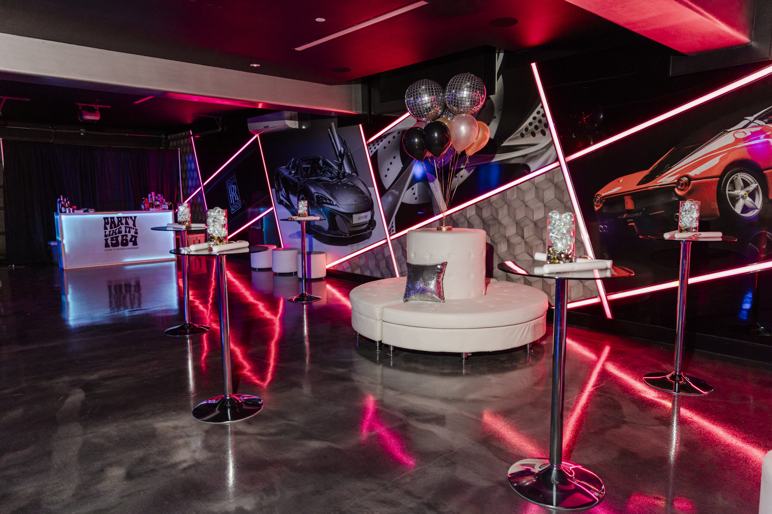 a room decorated for a birthday party with tables, balloons, disco balls, and a bar