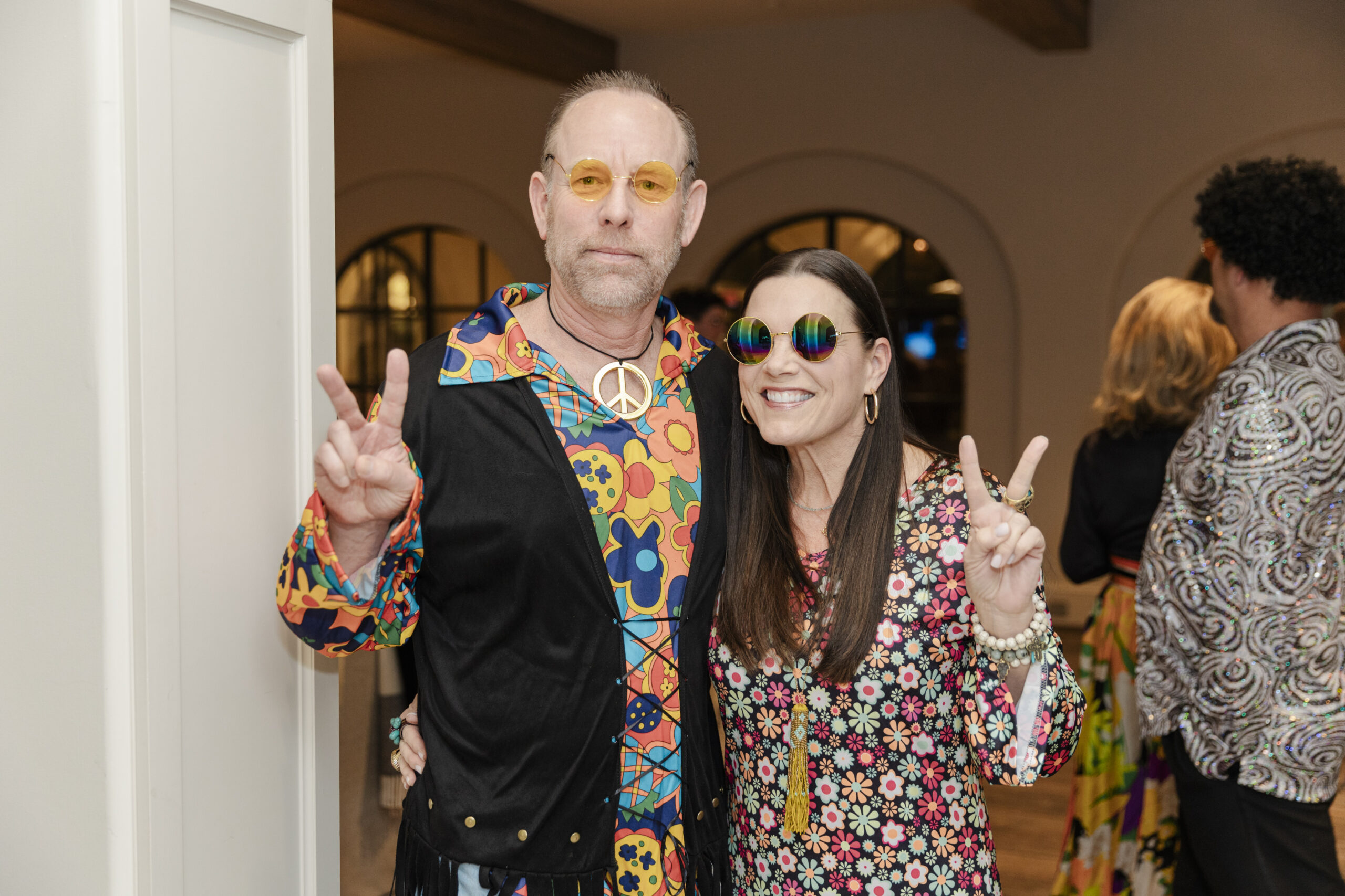 a man and woman posing and holding up peace signs at a 60's themed birthday party