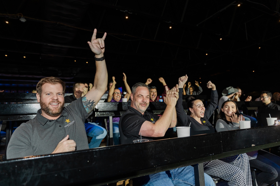 Fort Worth Event Photographer; Four event guests in the foreground celebrating with hand signs, clapping, and cheering