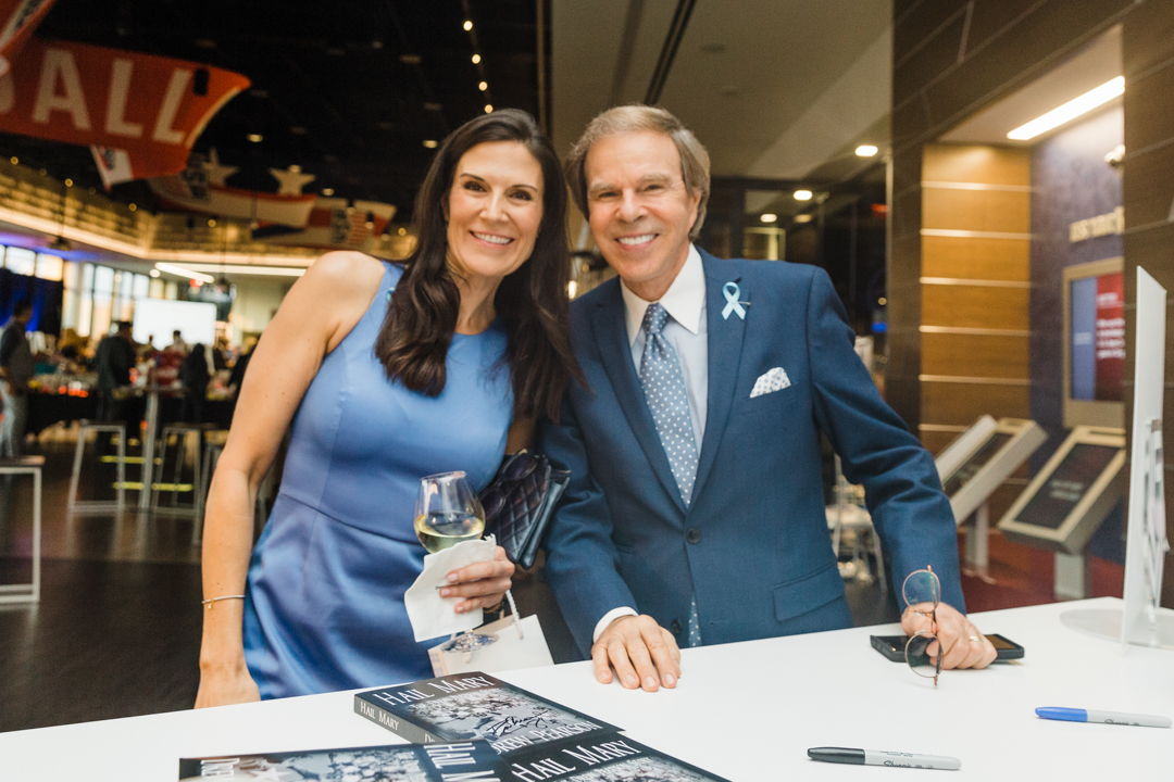 Fort Worth Fundraiser Event; photo of a man in a suit and woman in a dress smiling and posing for a photo while running a check in table at a fundraising event.