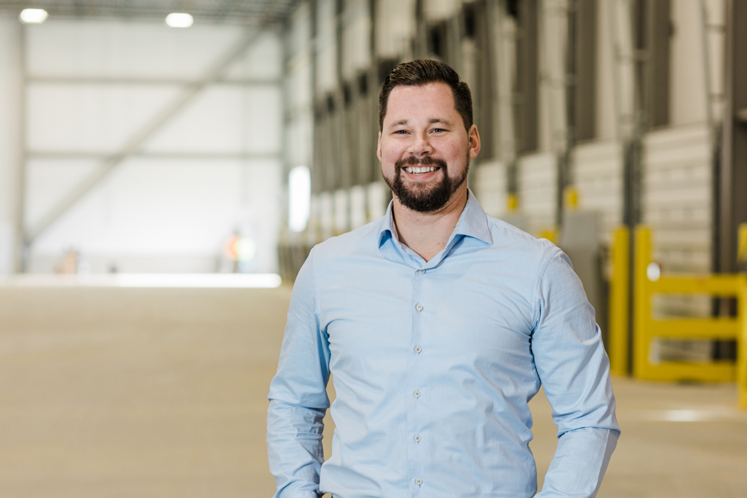 Fort Worth Headshot Photographer; Caucasian male with brown hair and a short brown beard wearing a light blue dress shirt in a large cold storage facility