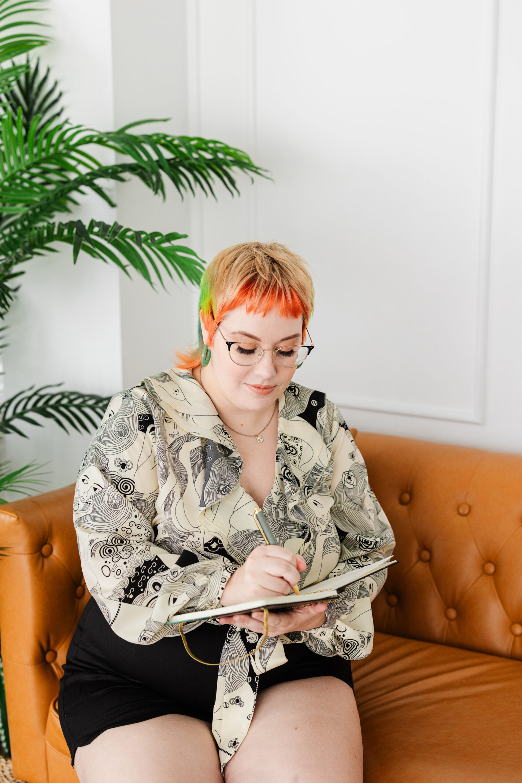 an author taking personal branding photos at new light studio in bedford texas she is sitting on an orange couch and writing in a notebook 