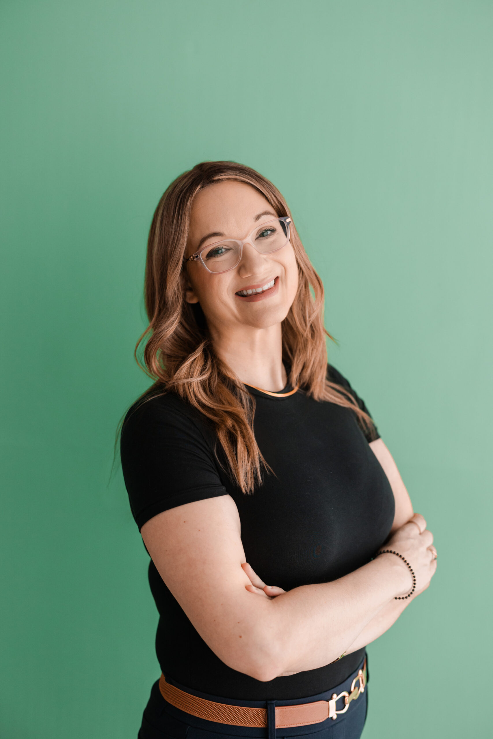 a woman wearing a black tshirt has her arms crossed in front of her and is standing in front of a green backdrop