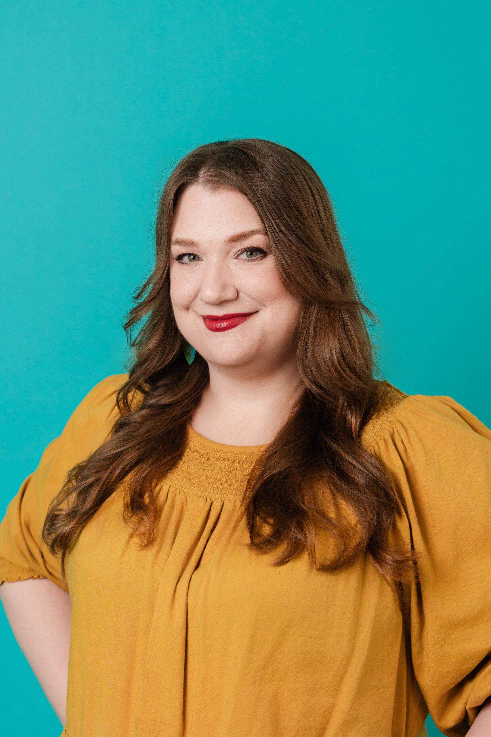 a woman wearing a yellow blouse taking a headshot in front of a teal backdrop