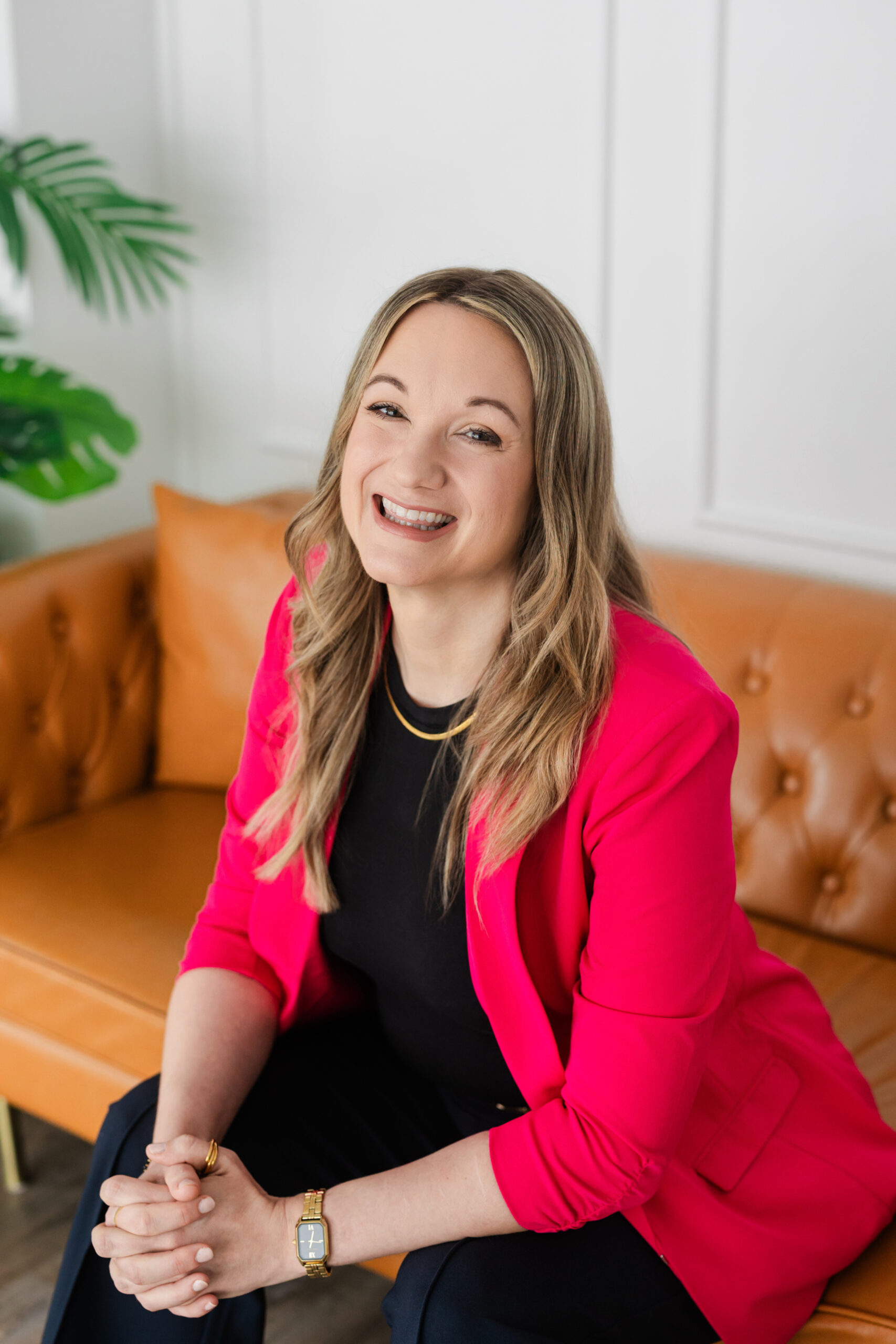 a woman sitting on an orange leather couch wearing a pink blazer and taking a professinal headshot in a studio
