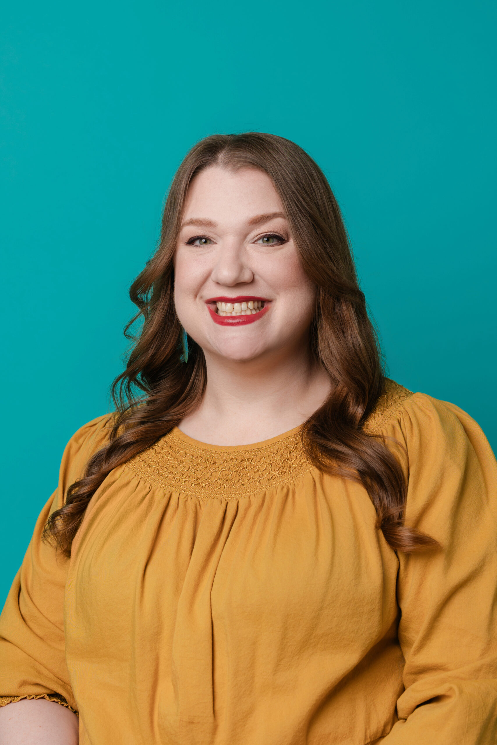 a woman wearing a yellow blouse taking a headshot in a studio in dallas with a blue backdrop