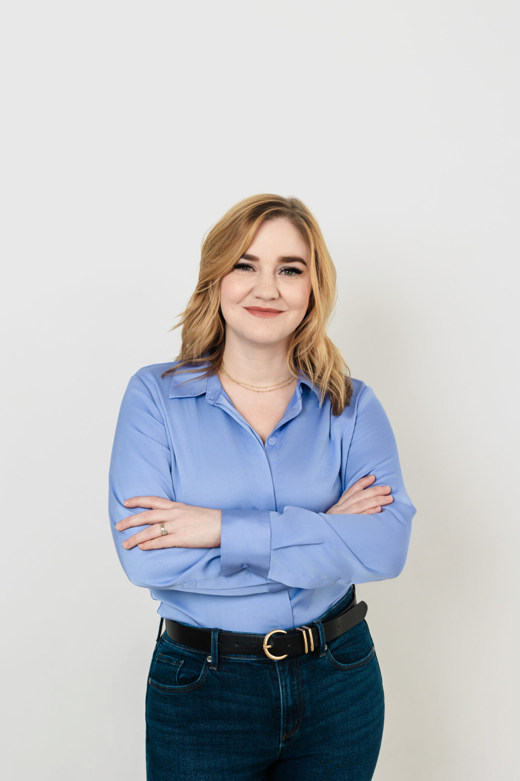 a woman wearing a blue button up and jeans taking a professional headshot in a studio