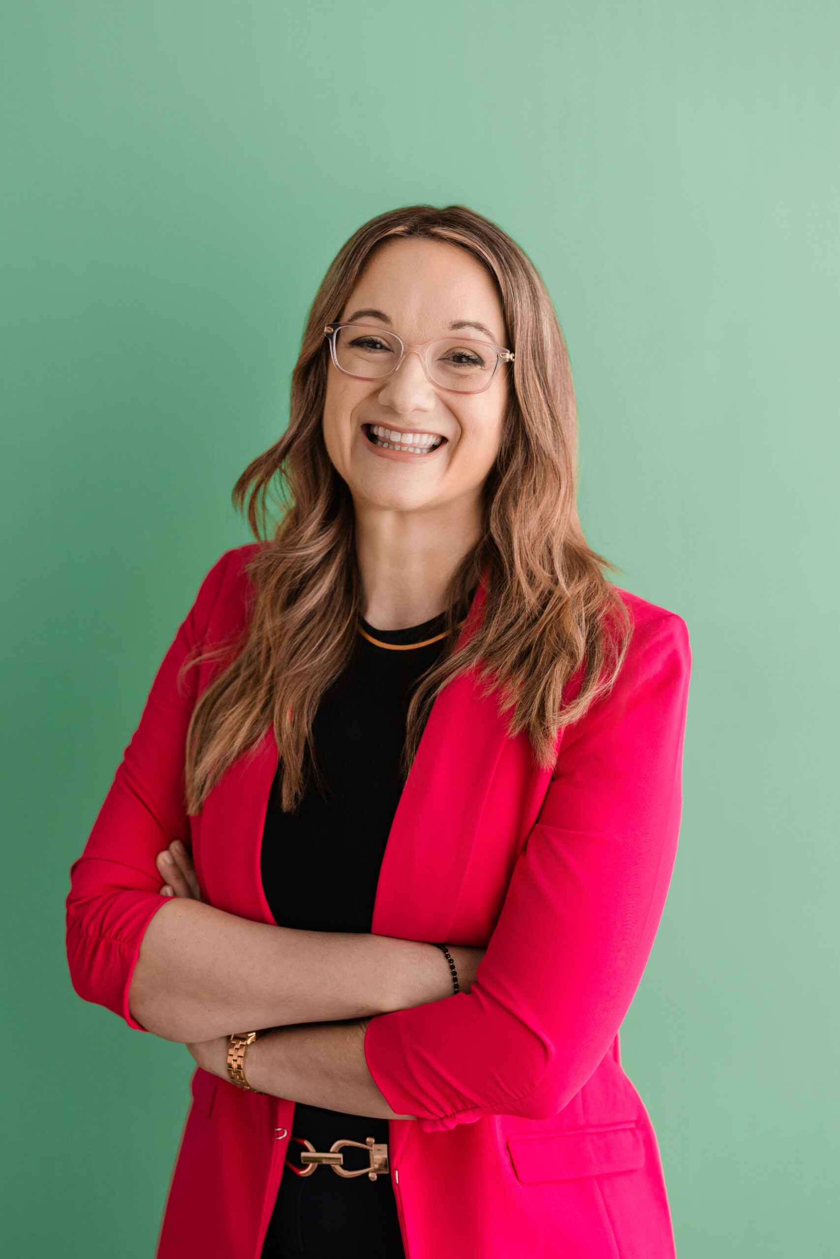 a woman standing with her arms crossed wearing a pink blazer and crossing her arms in front of her taking a headshot