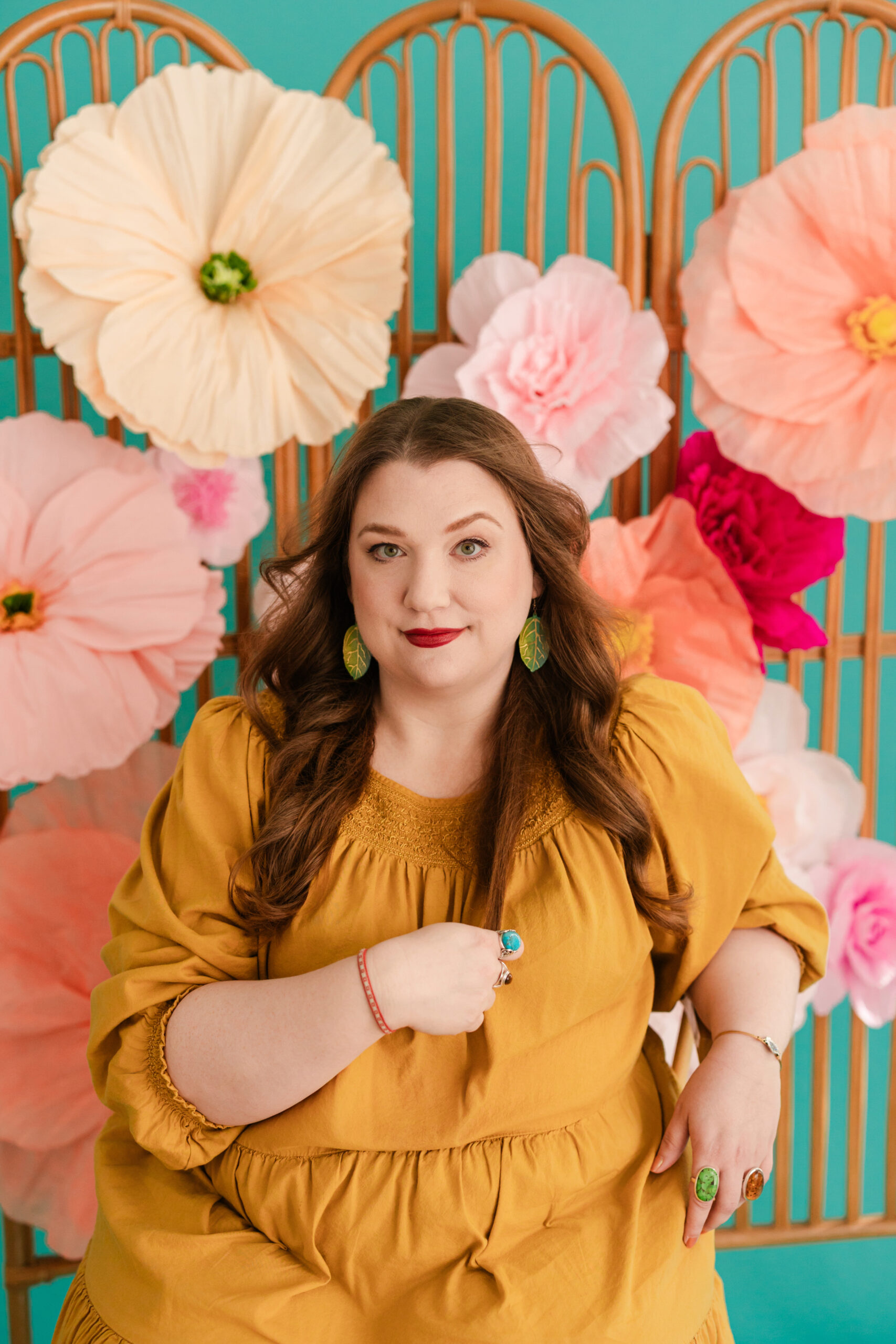 a woman sitting in a chair with a floral backdrop behind her