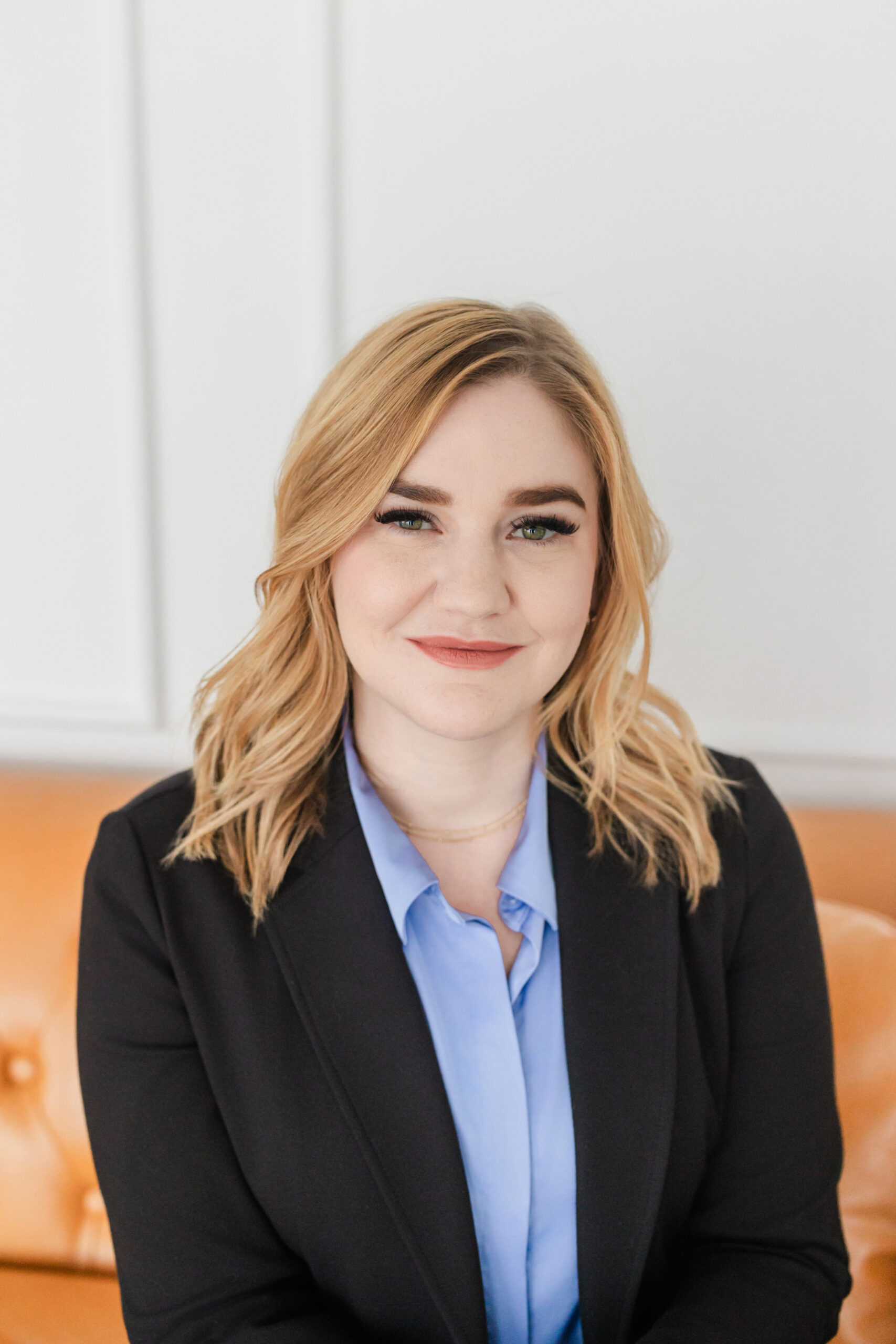 a woman sitting on an orange leather couch taking a professional headshot