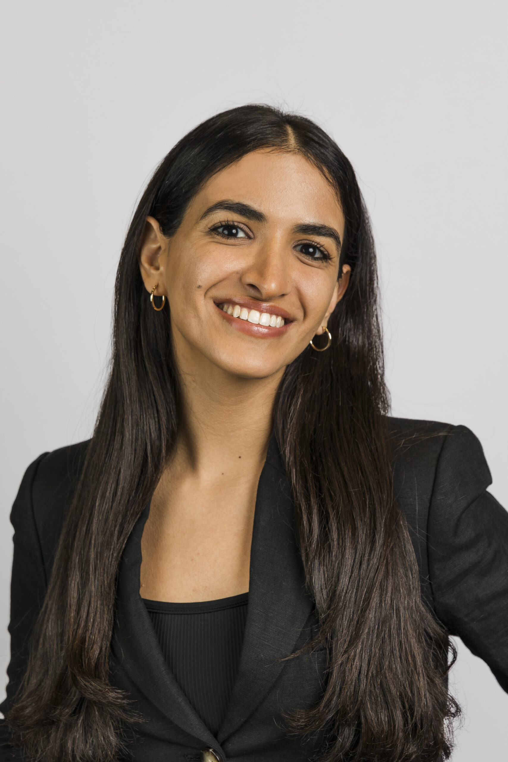 a woman wearing a black blazer and gold hoop earrings taking a corporate headshot 