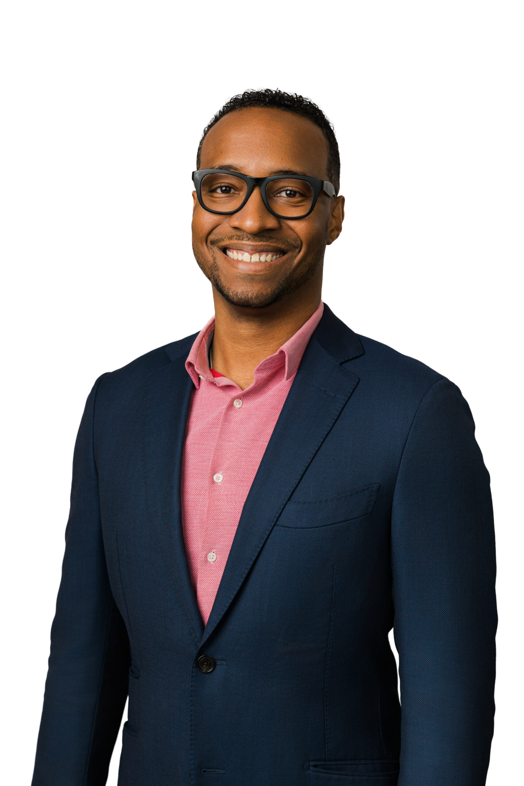 a man in a pink button up and navy blazer taking a corporate headshot against a white backdrop he is also wearing glasses 